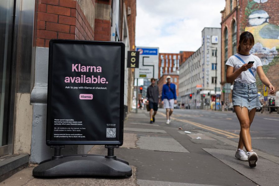 Members of the public pass by a floor advertisement for tech firm Klarna.